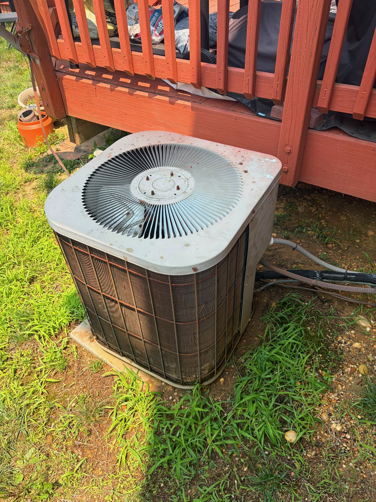 Older outdoor condenser beside a deck before replacement